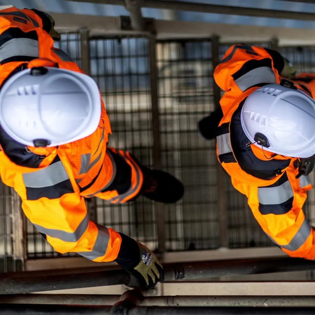 Aerial view of two workers in orange hi-vis and hard hats on stairs