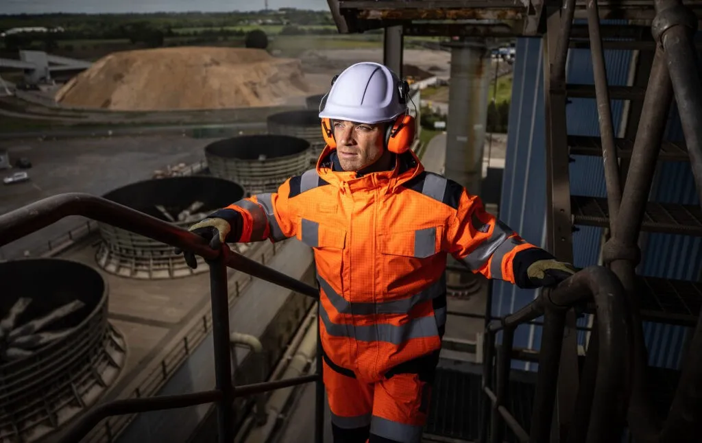 Worker in orange hi-vis and hard hat climbing stairs at industrial site