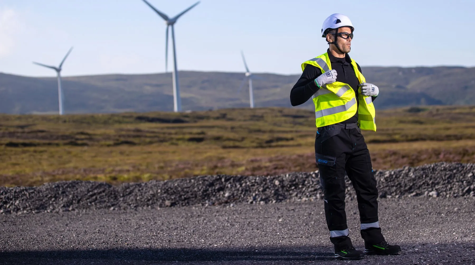 Worker in hi-vis vest standing in front of wind turbines