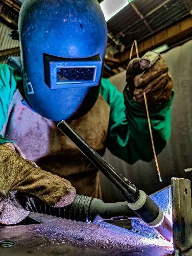 Welder in blue helmet welding metal in industrial workshop