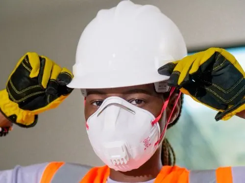 Construction worker wearing white hard hat, respirator mask, and safety gloves