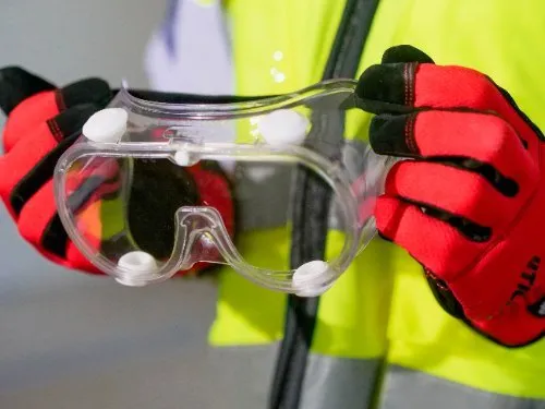 Worker in hi-vis vest holding clear safety goggles with red gloves