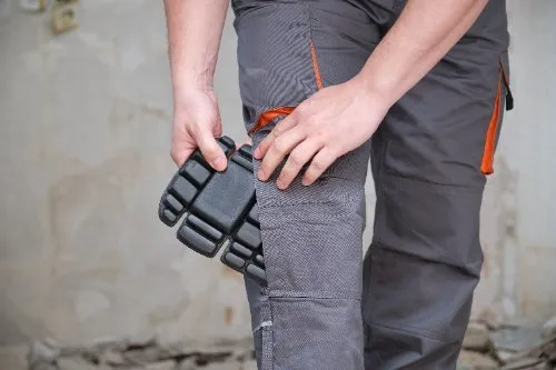 Worker adjusting knee pad on grey work trousers with orange detail