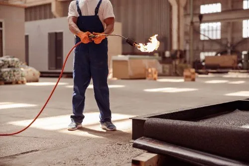 Worker in overalls using flame torch on metal surface in warehouse