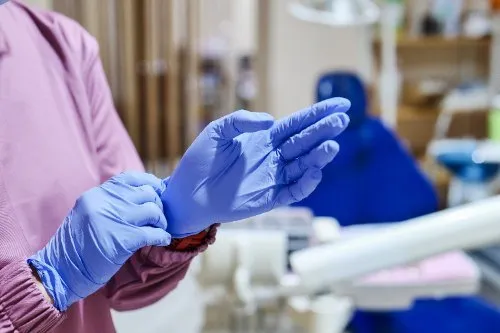 Dental professional putting on blue nitrile gloves in a clinic