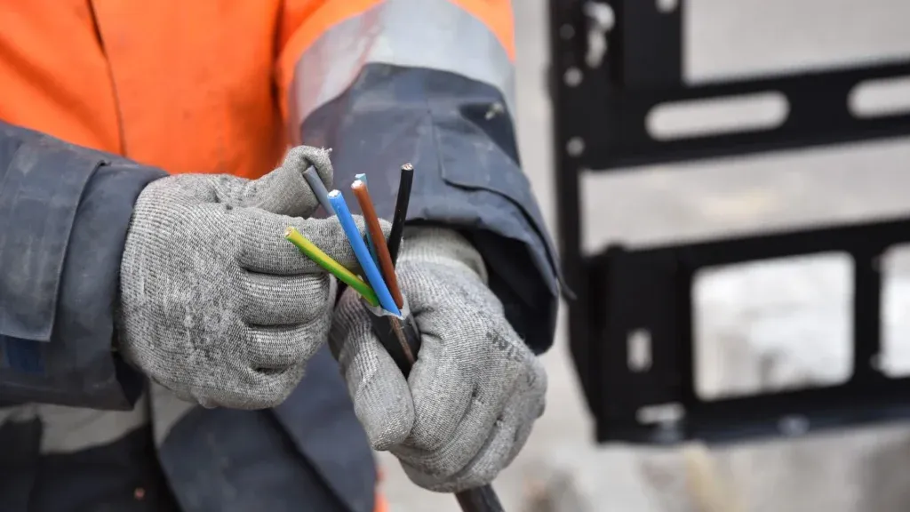 Electrician in grey gloves connecting multicoloured cables