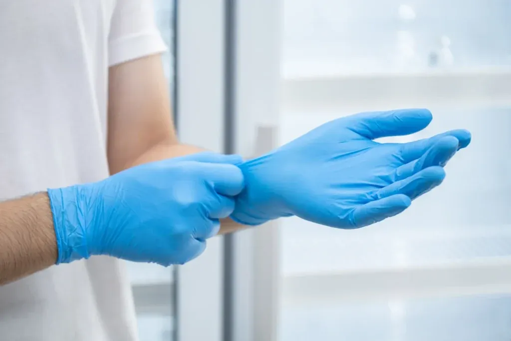 Doctor putting on blue nitrile gloves in clinical setting