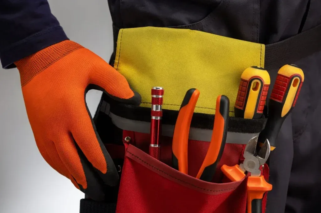 Electrician with orange gloves and tool belt holding electrical tools